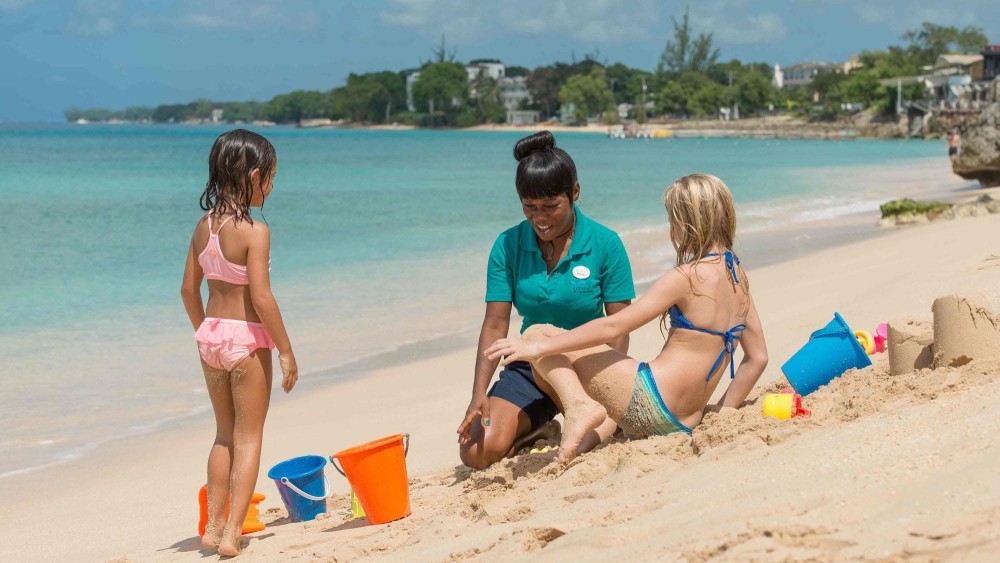 Female hotel employee playing with children at the beach at Crystal Cove by Elegant Hotels