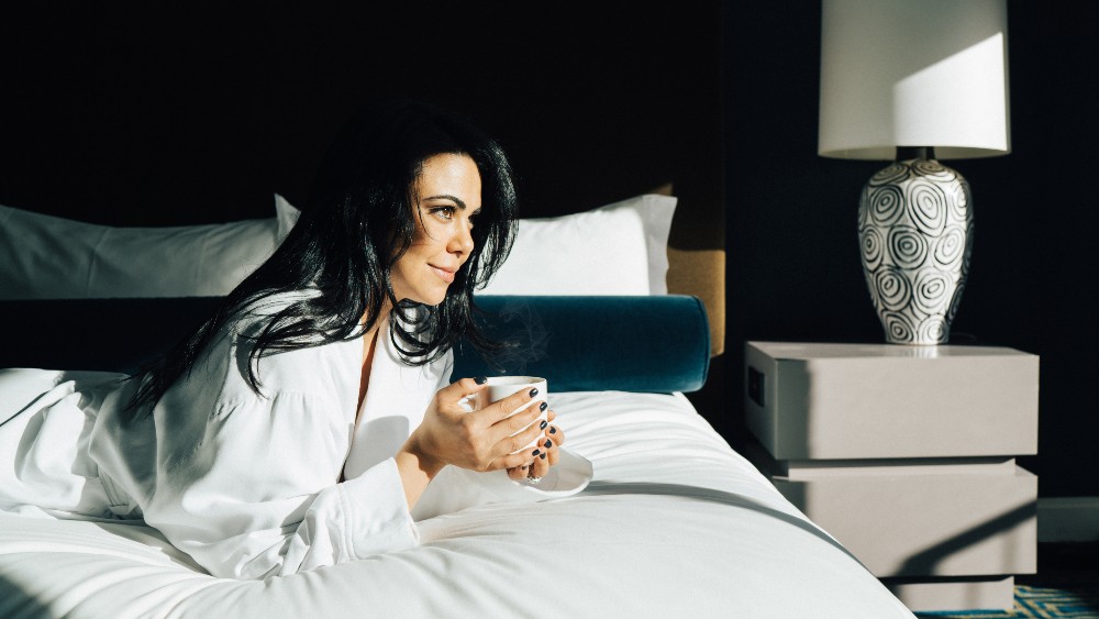 Woman with coffee on a bed at Loews Regency New York